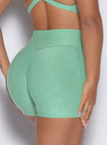 close up zommed in back view of a model wearing our tiny waist shorts in sage color along with the matching sports bra
