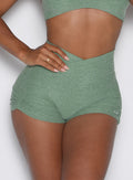close up front view of a model with one hand on the waist wearing the Tiny Waist Tie Shorts in basil color