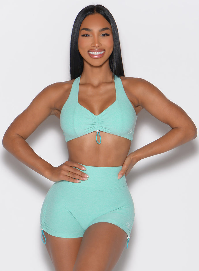 front profile view of a model with both hands on her waist wearing the Toggluxe bra in Oasis color