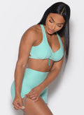 front right side profile view of a model adjusting the side toggle on the shorts wearing the Toggluxe bra in Oasis color