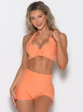 front profile view of a model with one hand on the strap wearing the Toggluxe bra in Tangerelle color