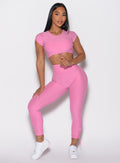 front profile view of a model holding the front toggle on the top wearing the Toggle Pull Leggings in Bubblegum color