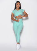 front profile view of a model holding the front toggle of the top and looking to the left wearing the Toggle Pull Leggings in Oasis color