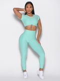front profile view of a model holding her hair on the back with one hand wearing the Toggle Pull Leggings in Oasis color