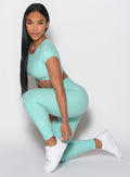 left side profile view of a model in a kneeling pose wearing the Toggle Pull Leggings in Oasis color