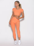 front profile view of  model holding the front toggle and looking to the left side wearing the Toggle Pull Leggings in Tangerelle color 