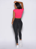 back profile view of a model facing to the left side and one hand resting on top of her head wearing the Bombshell Era Tee in solid victory ruby color 