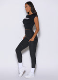 left side profile view of a model wearing the Bombshell Era Tee in black color  paired with the matching leggings 