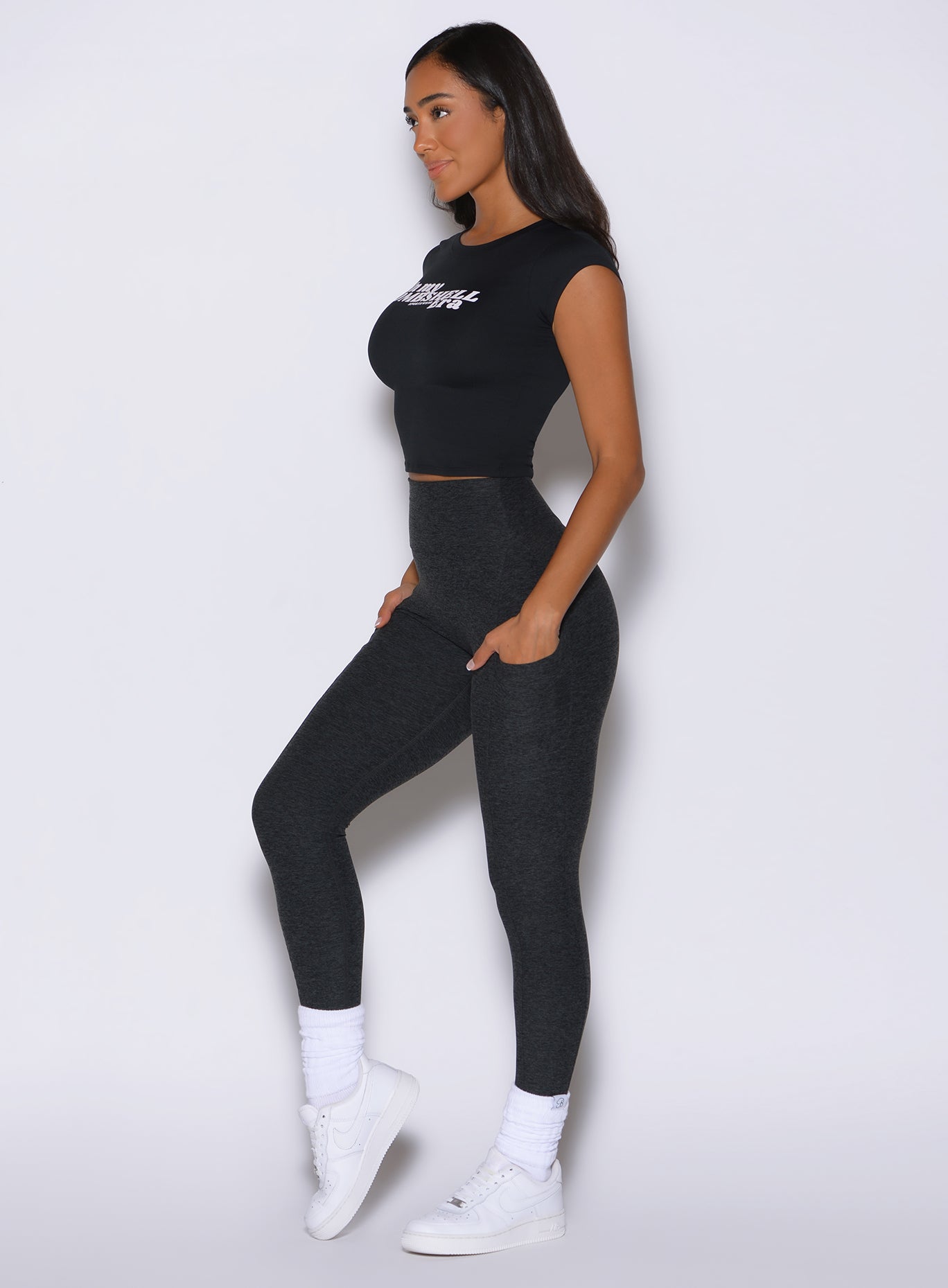 left side profile view of a model wearing the Bombshell Era Tee in black color  paired with the matching leggings 