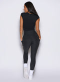 back profile view of a model with both hands inside the pockets of the leggings wearing the Bombshell Era Tee in black color 