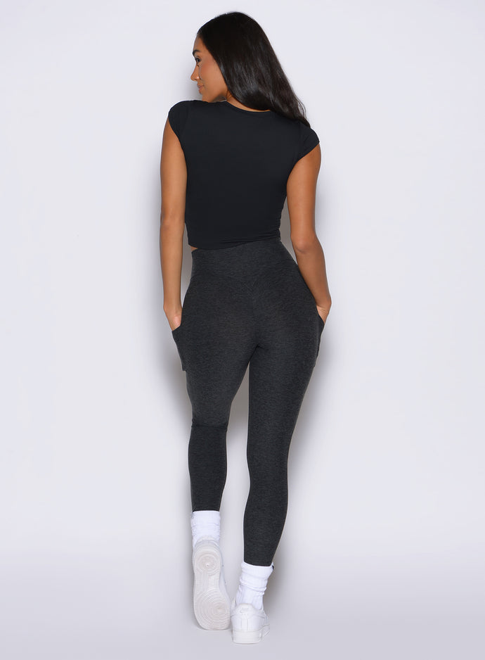back profile view of a model with both hands inside the pockets of the leggings wearing the Bombshell Era Tee in black color 
