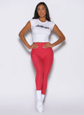 front view of a model wearing the Bombshell Era Tee in white color paired with a red leggings 