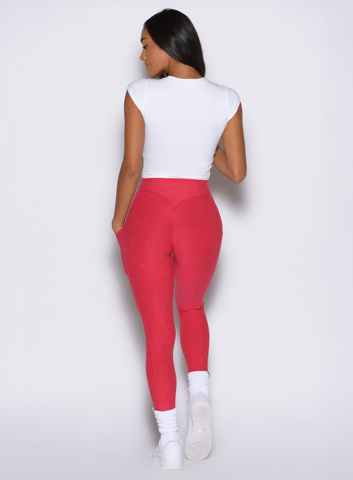 back profile view of a model wearing the Bombshell Era Tee in white color  paired with a red leggings 