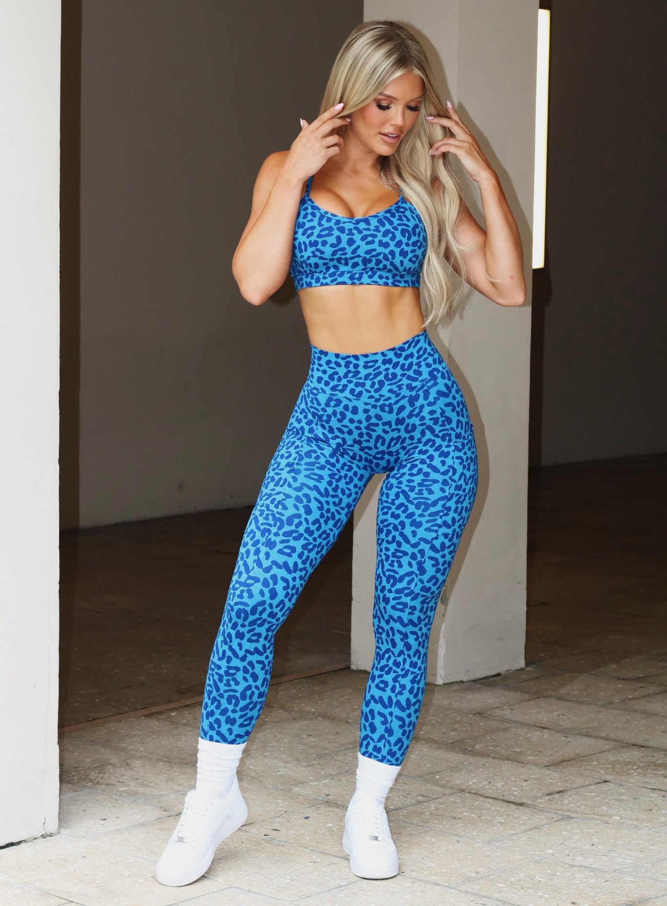 Front profile view of a model wearing our pumped sports bra in blue cheetah color and matching bombshell leggings