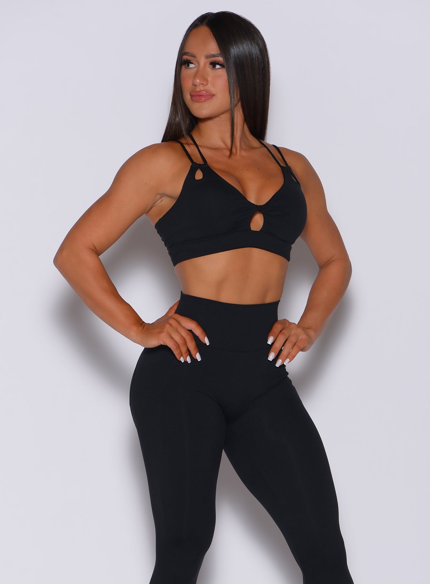 Front profile view of a model with her hands on waist wearing our black twist sports bra and a matching high waistedleggings