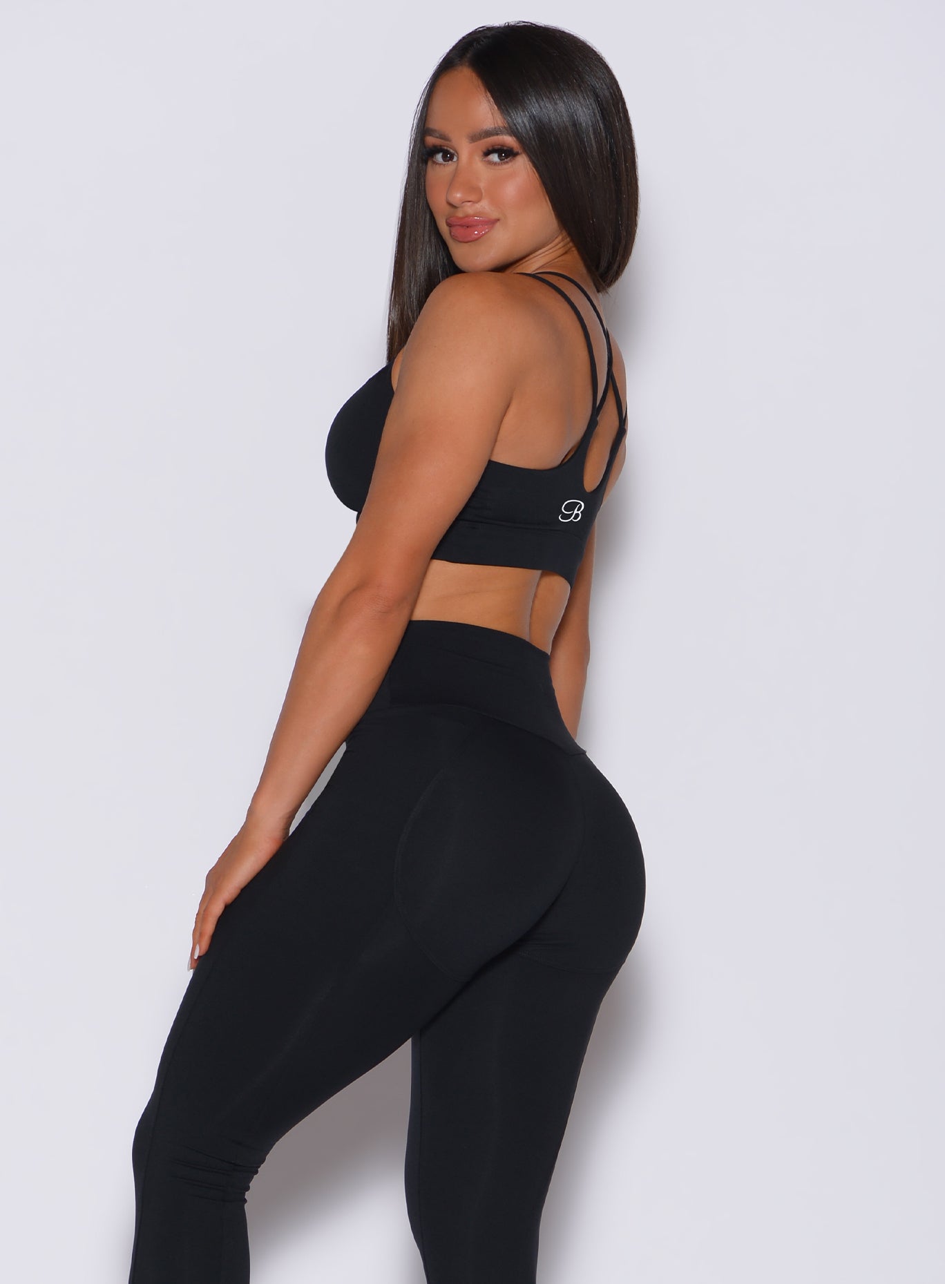 Left side profile view of a model facing to her left wearing our black twist sports bra and a matching leggings