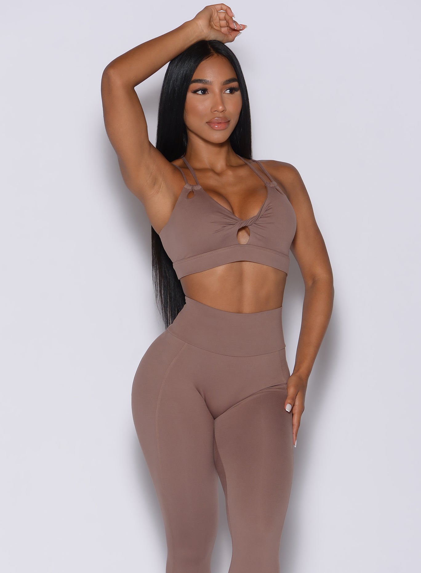 front profile view of a model with her right hand on her head wearing our twist sports bra in tan color and a matching leggings