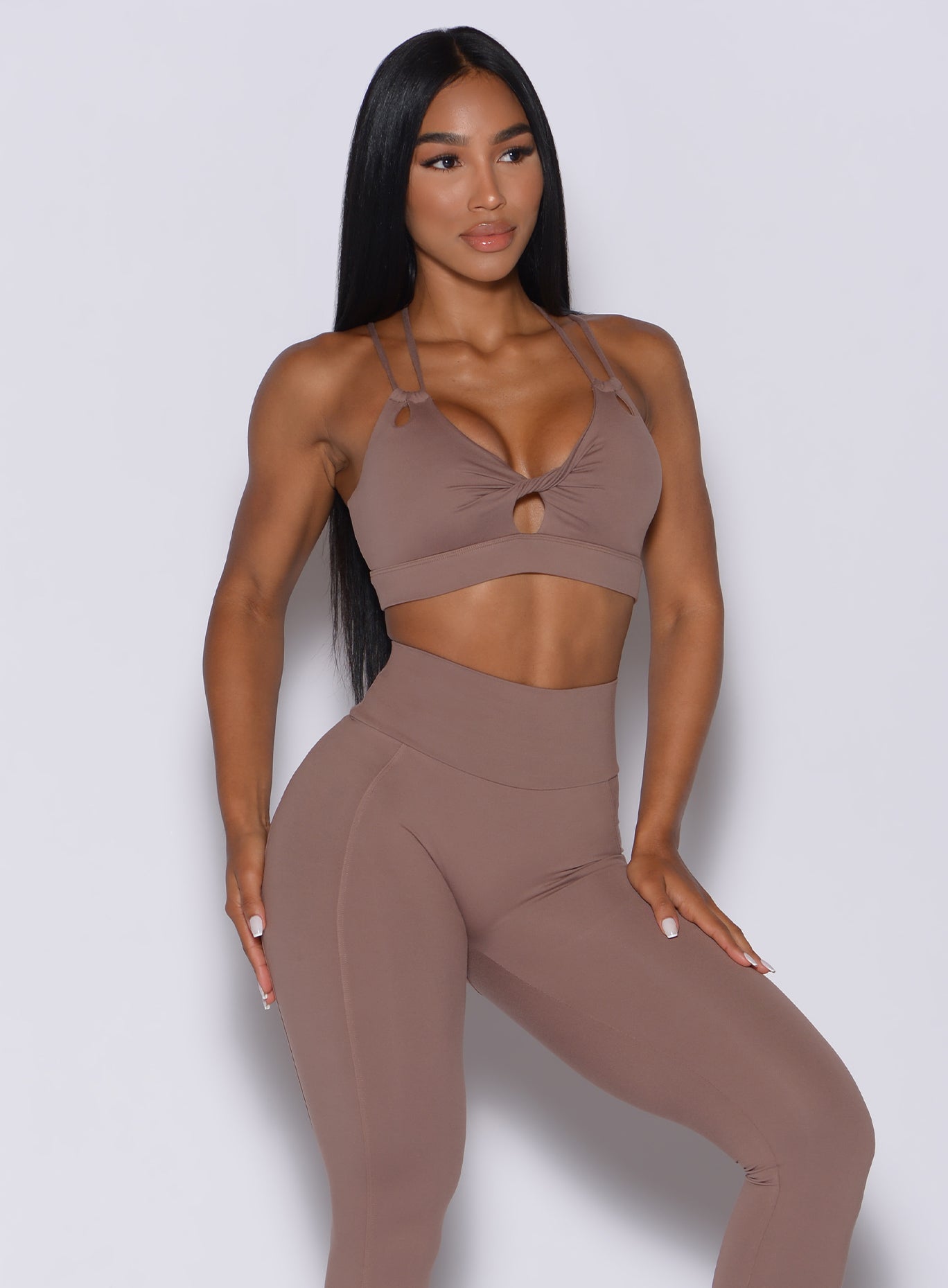 Front profile view of a model in our twist sports bra in tan color and a matching bombshell leggings