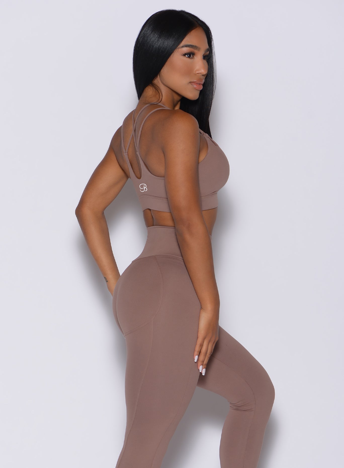 Right side profile view of a model in our twist sports bra in tan color and a matching leggings