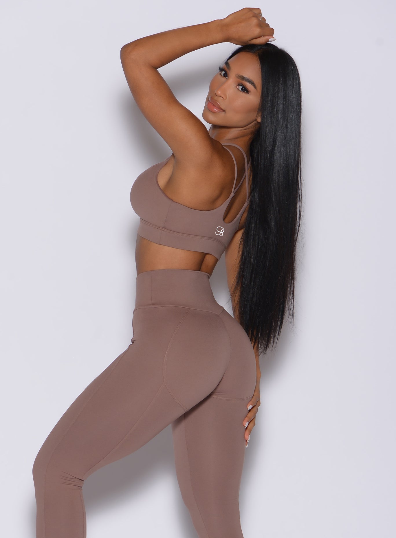 Left side profile view of a model in our twist sports bra in tan color and a matching leggings