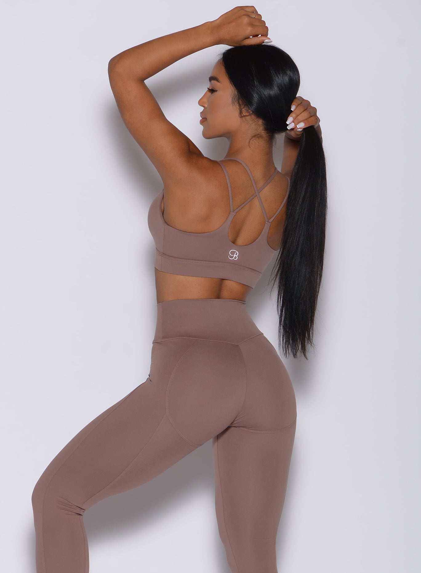 Back profile view of a model wearing our twist sports bra in tan color and a matching leggings