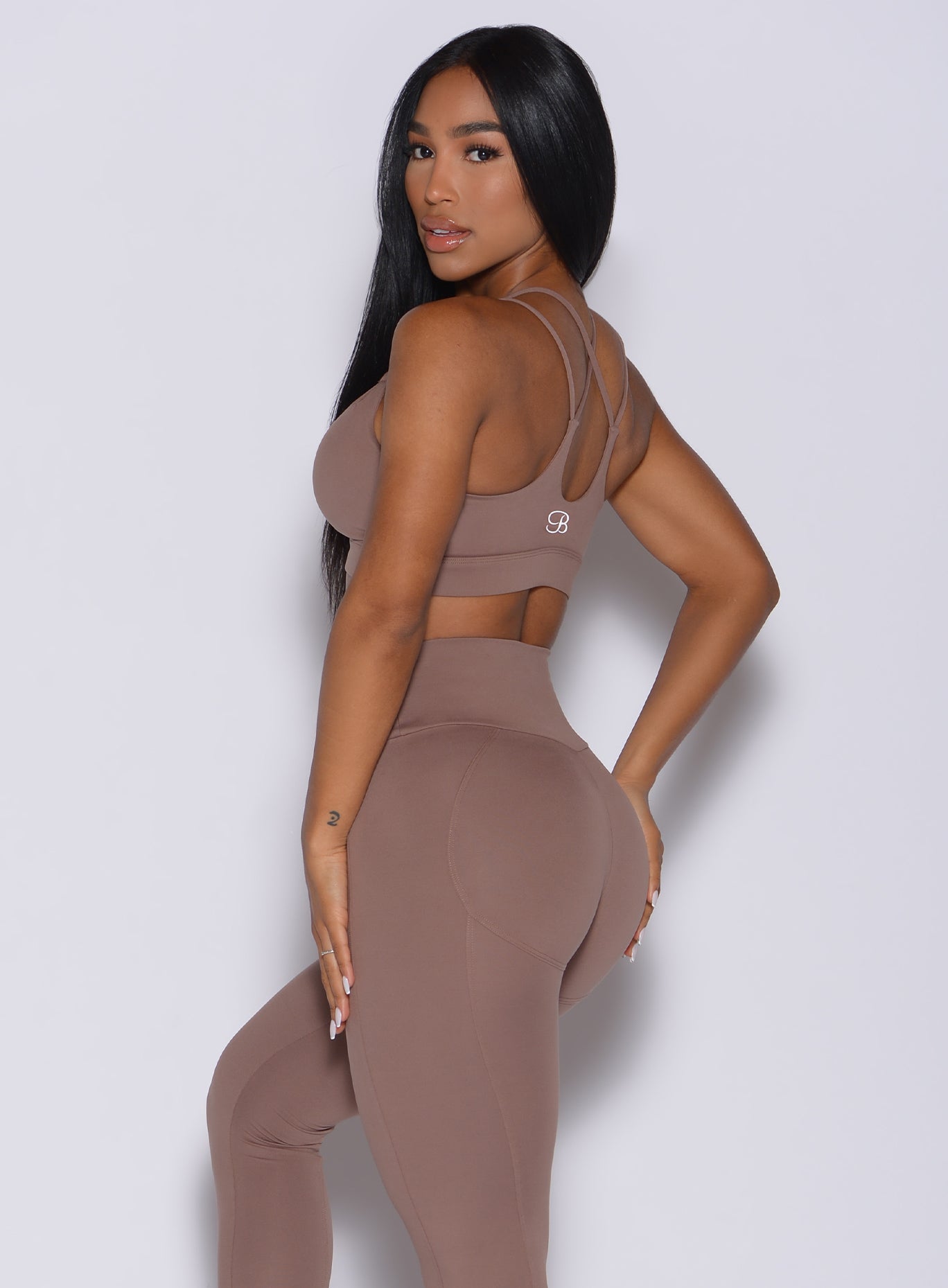 Left side profile view of a model facing to her left wearing our twist sports bra in tan color and a matching leggings