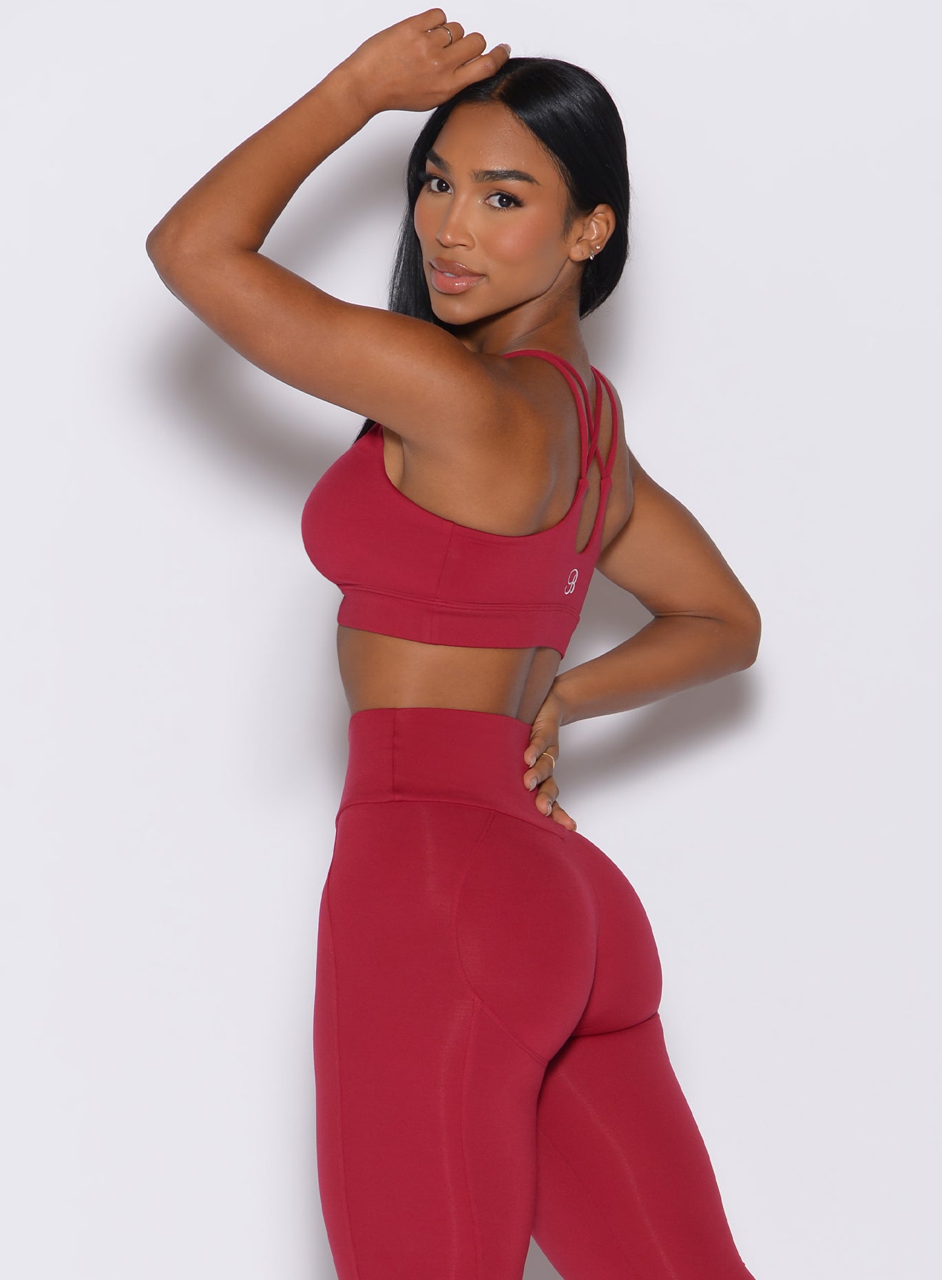Left side profile view of a model facing to her left wearing our twist sports bra in maroon color along with a matching leggings