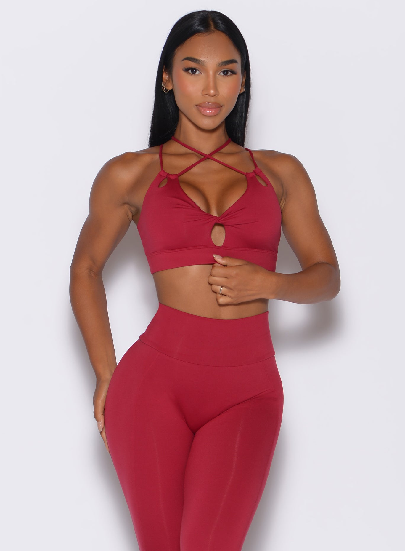 Front profile view of a model wearing our twist sports bra in maroon color along with a matching leggings 