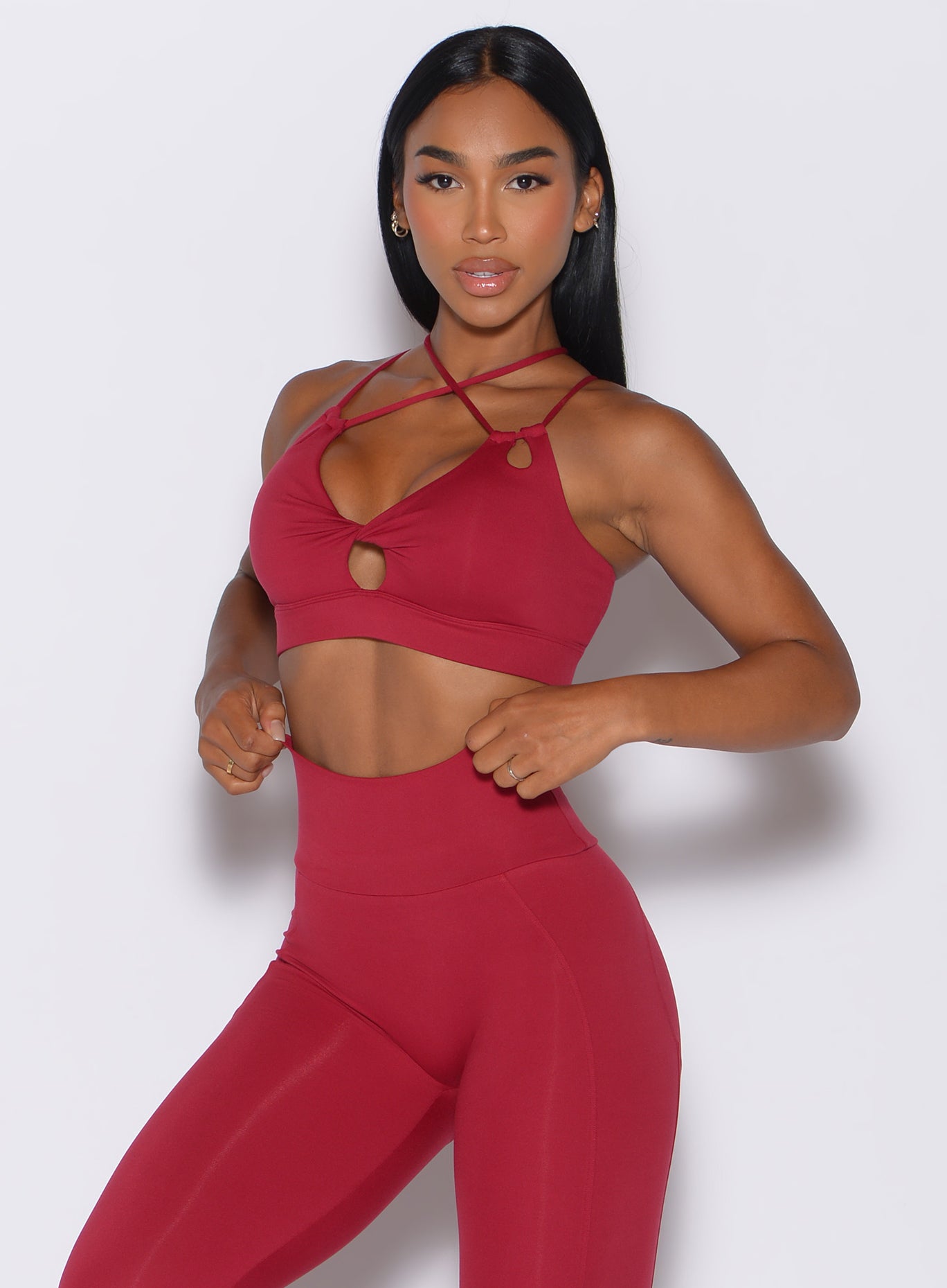 Front profile view of a model wearing our twist sports bra in maroon color along with a matching shape leggings