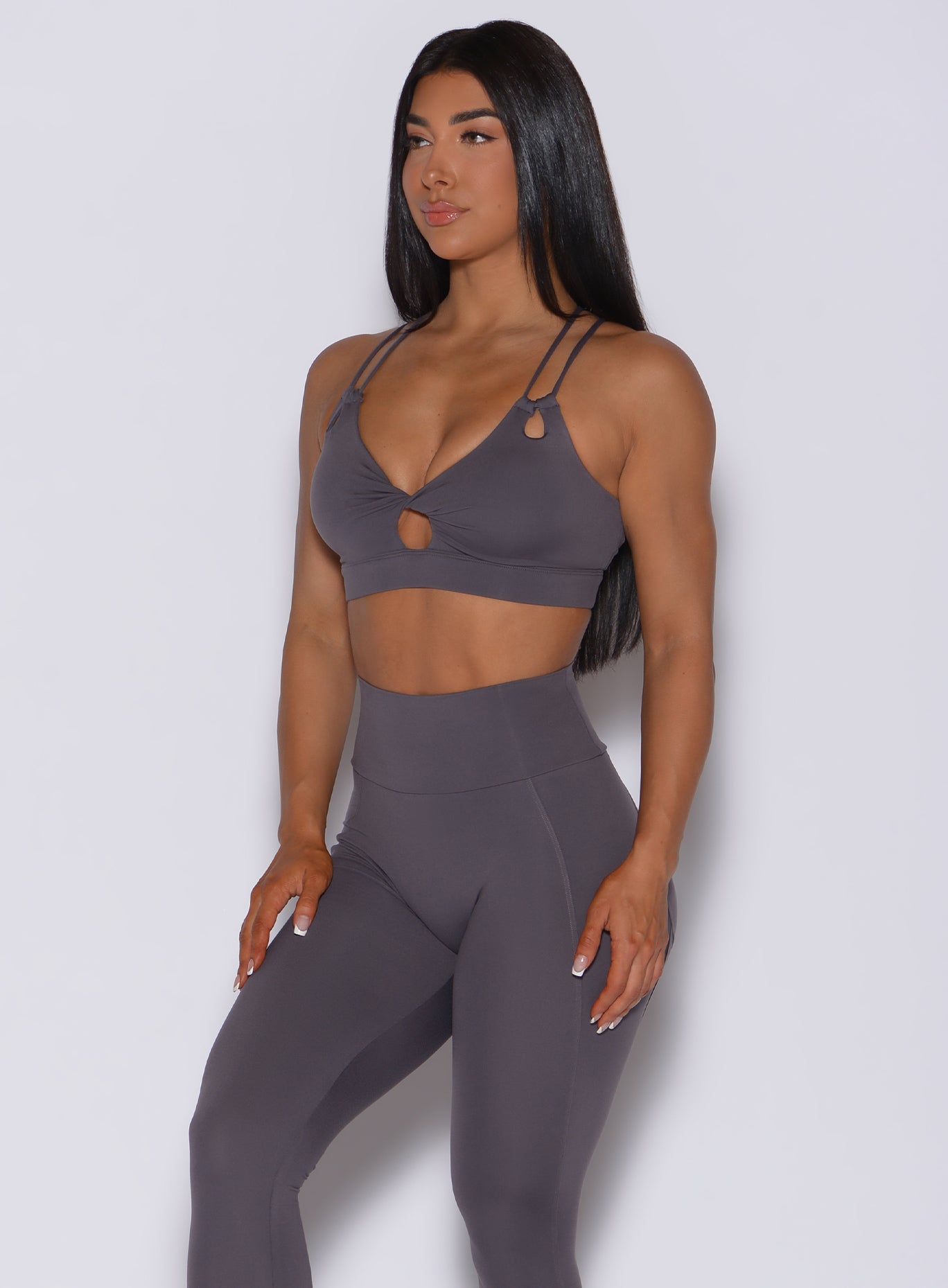 Front profile view of a model in our twist sports bra in gray smoke color and a matching leggings