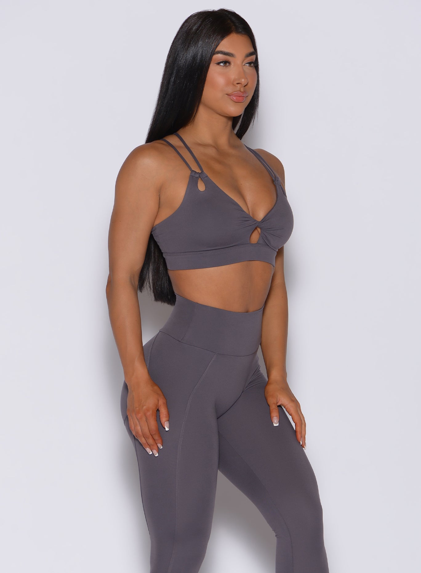 Left side profile view of a model in our twist sports bra in gray smoke color and a matching leggings