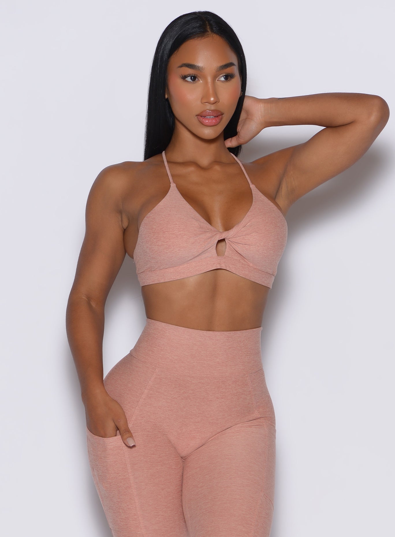 front profile picture of a model wearing our tiny twist bra in nude sand color along with the matching curves leggings