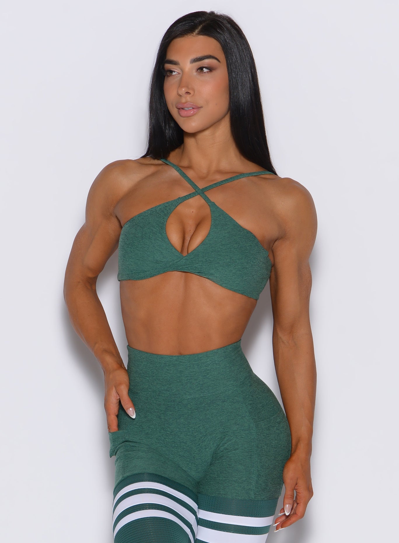 Front profile view of a model wearing our twist mini bra in emerald green color along with a matching thigh high leggings