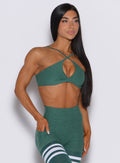 Front profile view of a model with her right hand in pocket wearing our twist mini bra in emerald green color along with a matching thigh high leggings