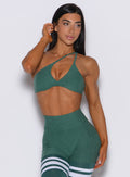 Front profile picture of a model facing forward wearing our twist mini bra in emerald green color along with a matching thigh high leggings
