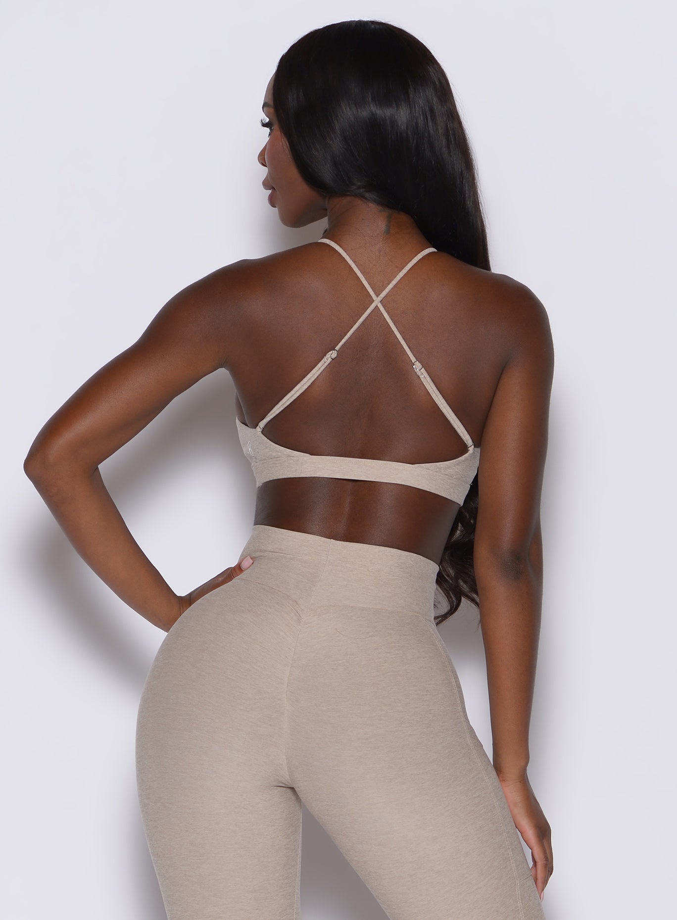 back profile view of a model facing to her left wearing our tiny twist bra in taupe color along with the matching curves leggings