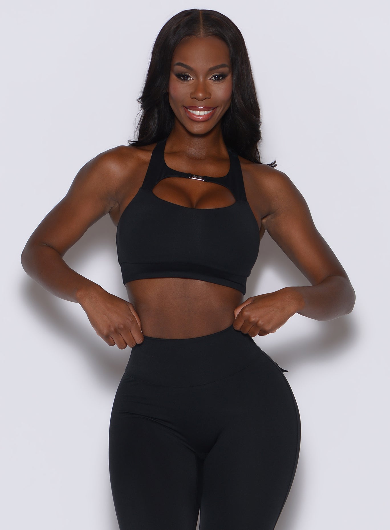 front profile view of a model smiling and wearing our black two way bra along with the matching leggings