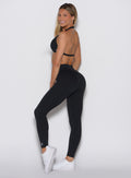 left side profile view of a model looking over her shoulder wearing our Uplift Peach Leggings in black color