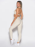 left side profile view of a model looking over her shoulder wearing the Uplift peach leggings in pearl white color