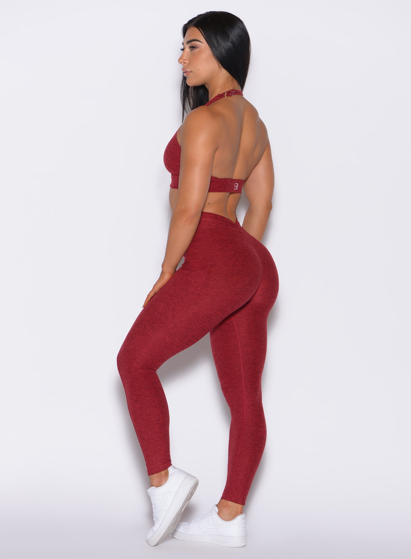 Left side profile view of a model in our V Back Leggings in garnet red color along with the matching bra