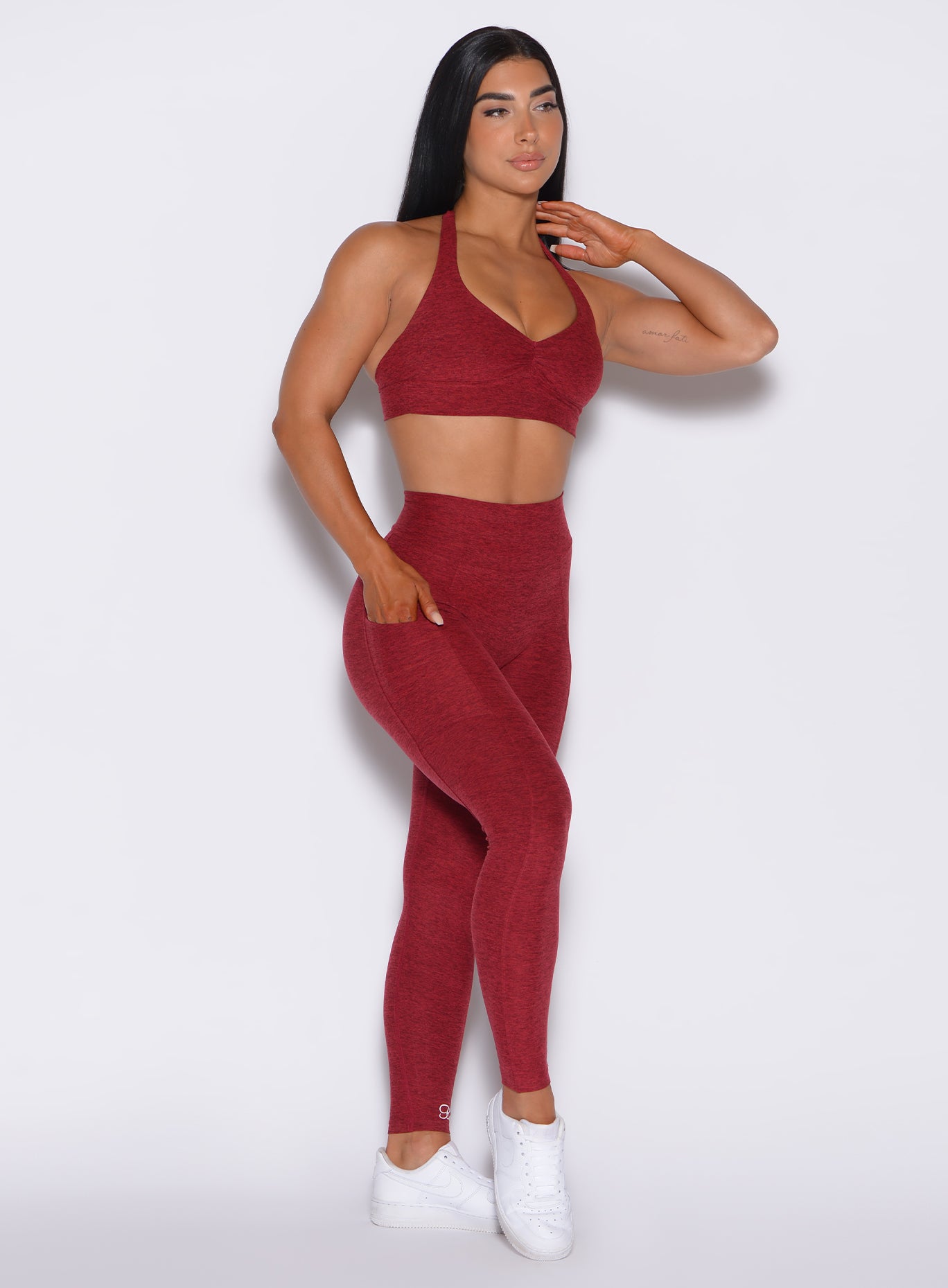 front profile view of a model with her right hand in pocket wearing our V Back Leggings in garnet red along with the matching bra