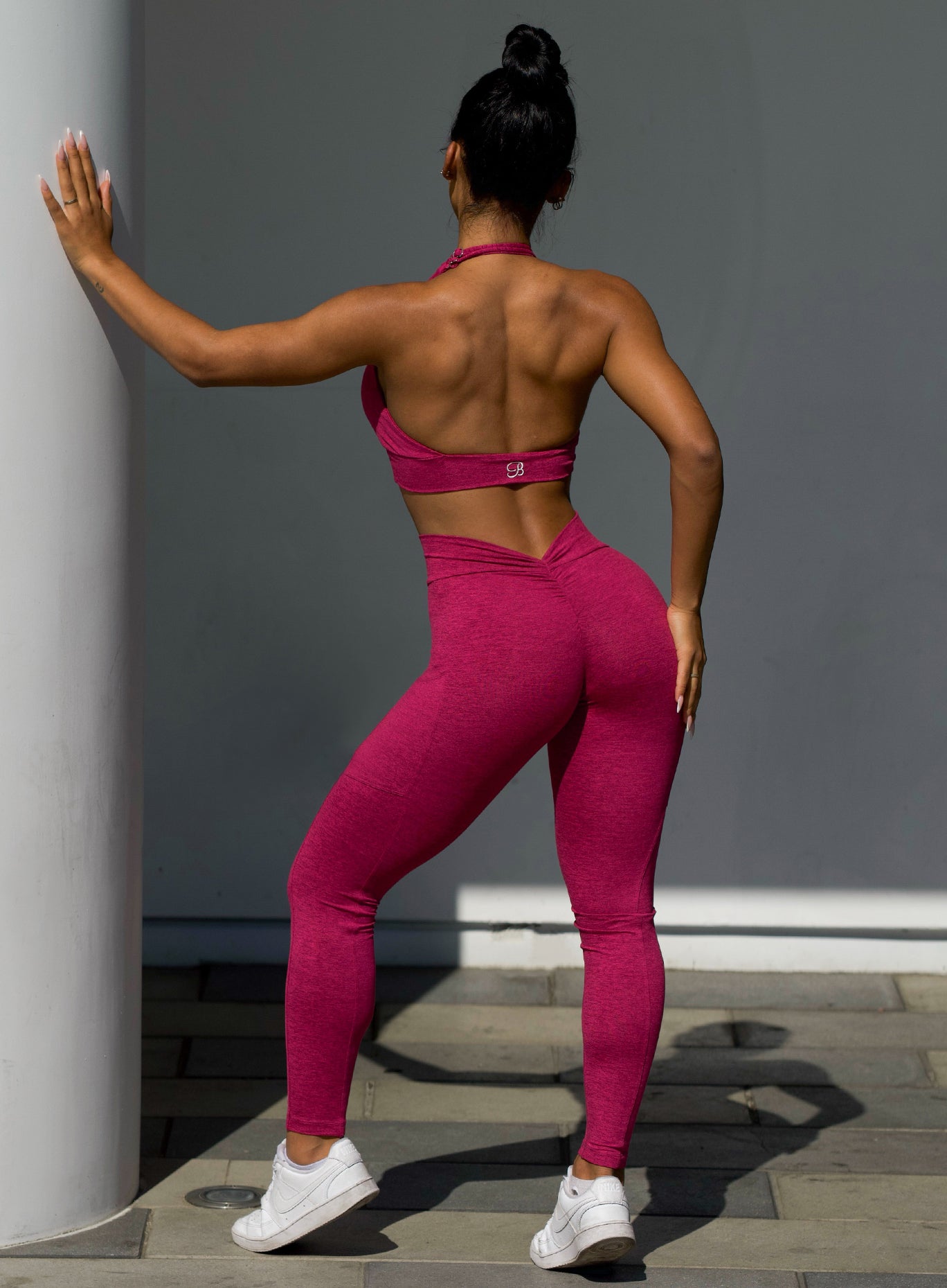 back profile view of a model outside wearing  our V back leggings in fuchsia color along with the matching bra