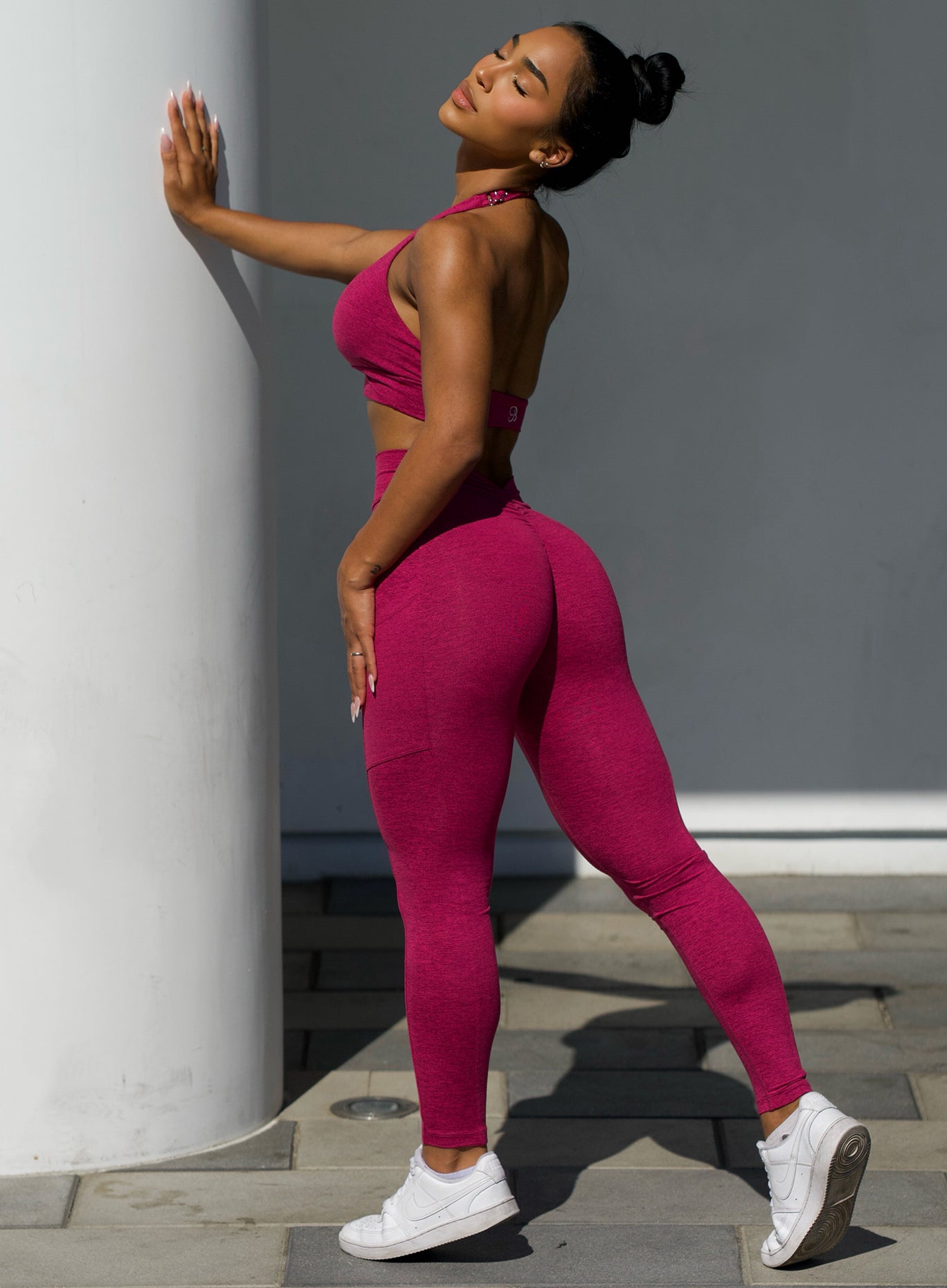 side profile view of a model outside wearing our V back leggings in fuchsia color along with the matching bra