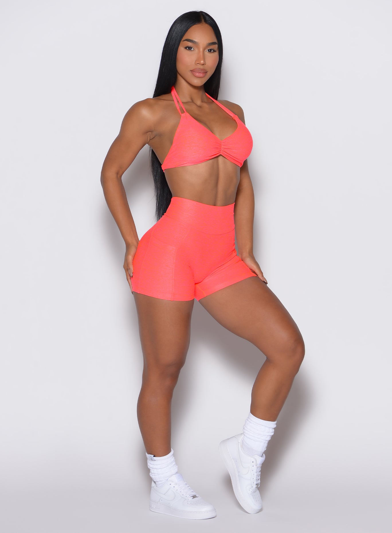 front profile picture of a model wearing our V back shorts in Neon Apricot Pink color along with the matching sports bra