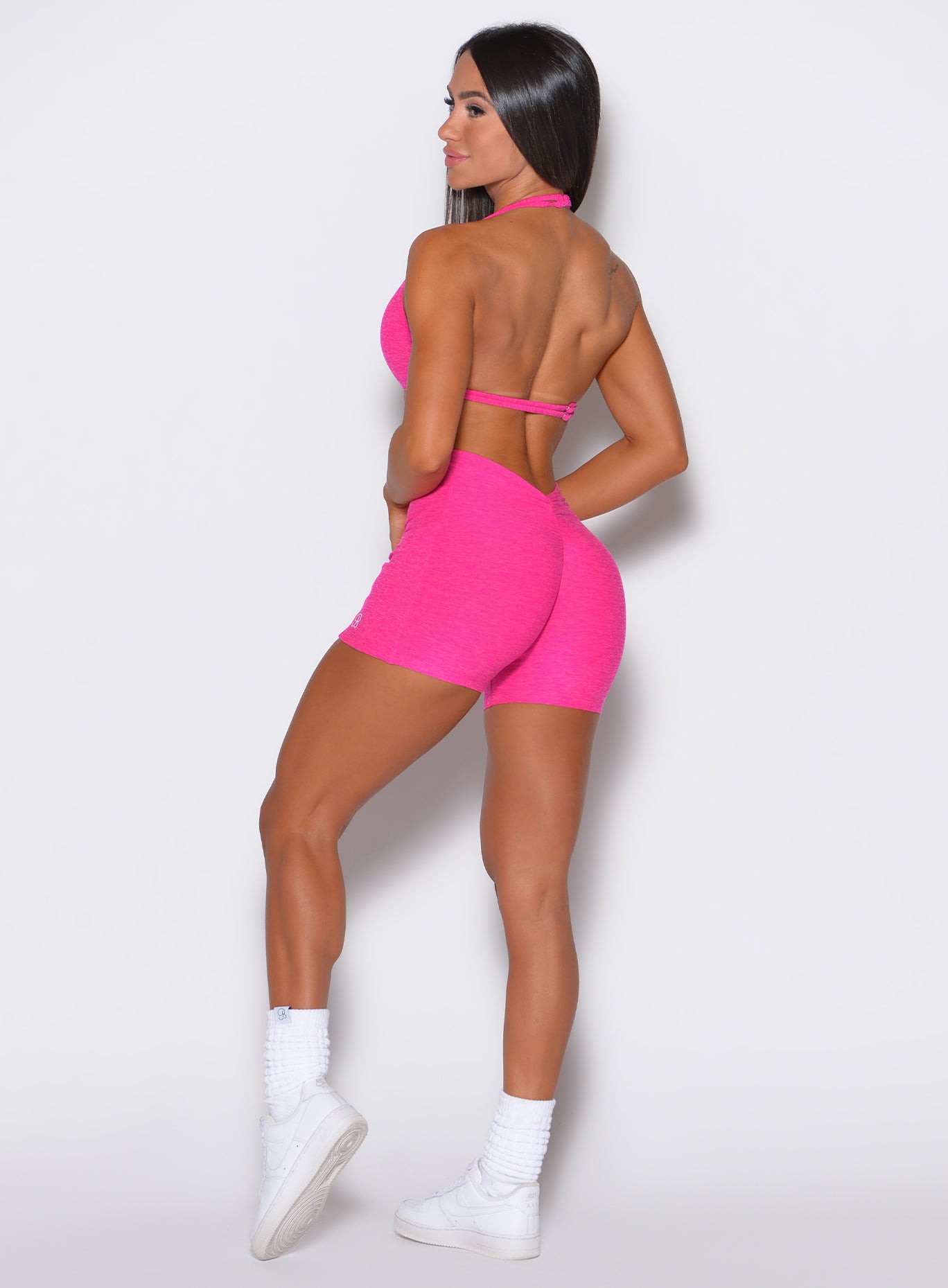 left side profile picture of a model facing to her left  wearing our V back shorts in Neon Pink Berry color along with the matching sports bra