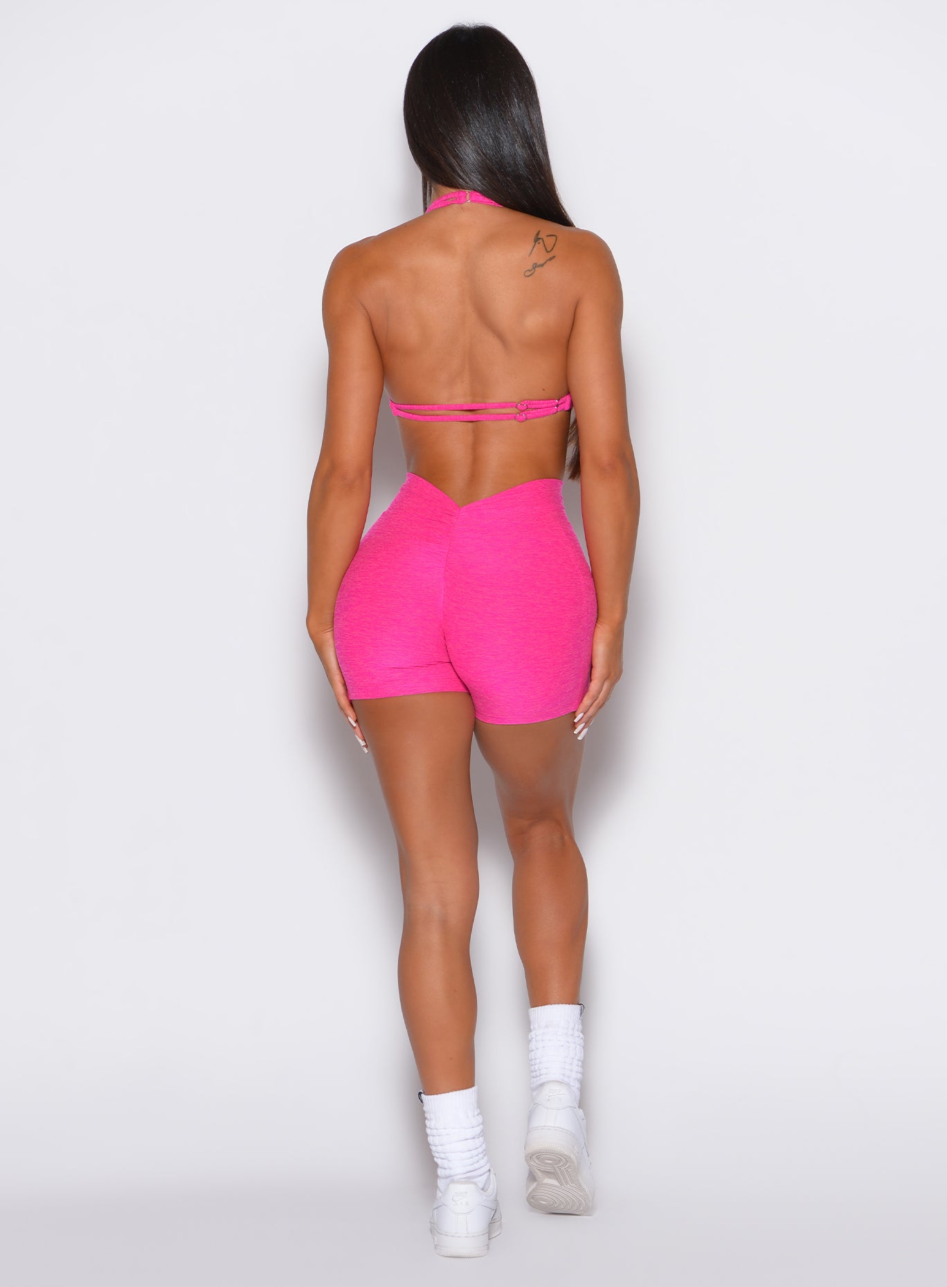 back profile view of a model wearing our V back shorts in Neon Pink Berry color along with the matching bra
