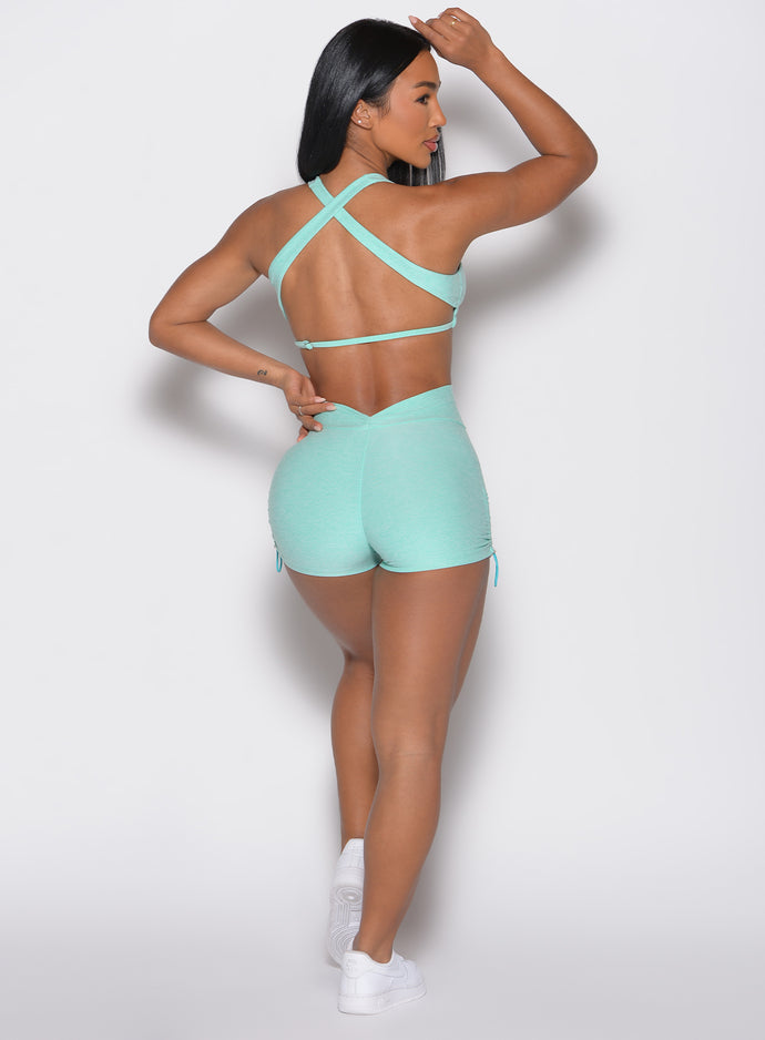 back profile view of a model with one hand resting on top of her head and the other hand on her waist wearing the V back toggle shorts in Oasis color
