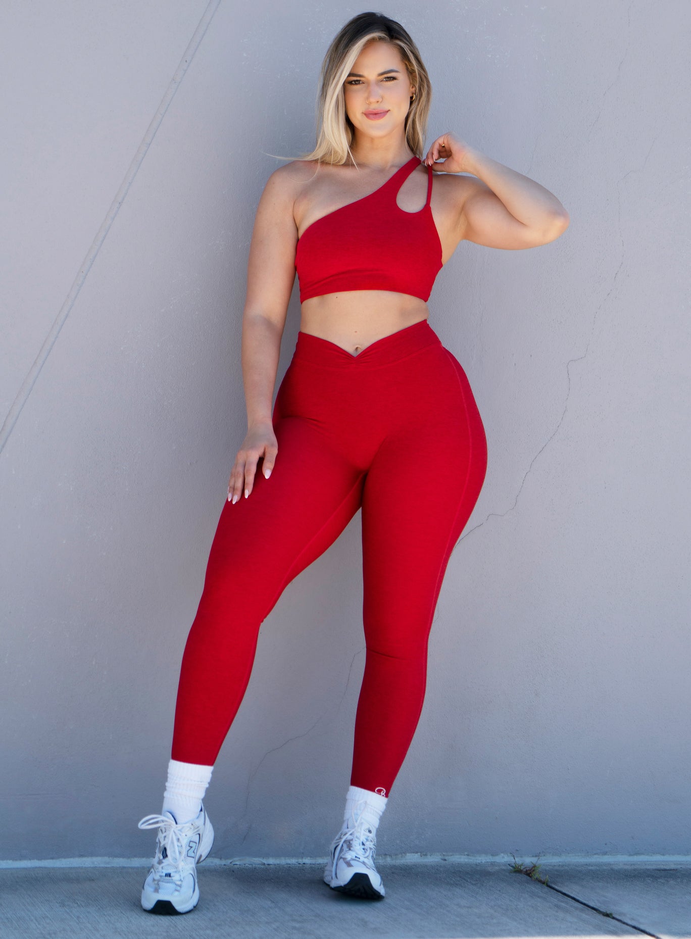 front profile view of a model adjusting her bra strap wearing our V Active Leggings in scarlet red along with the matching top