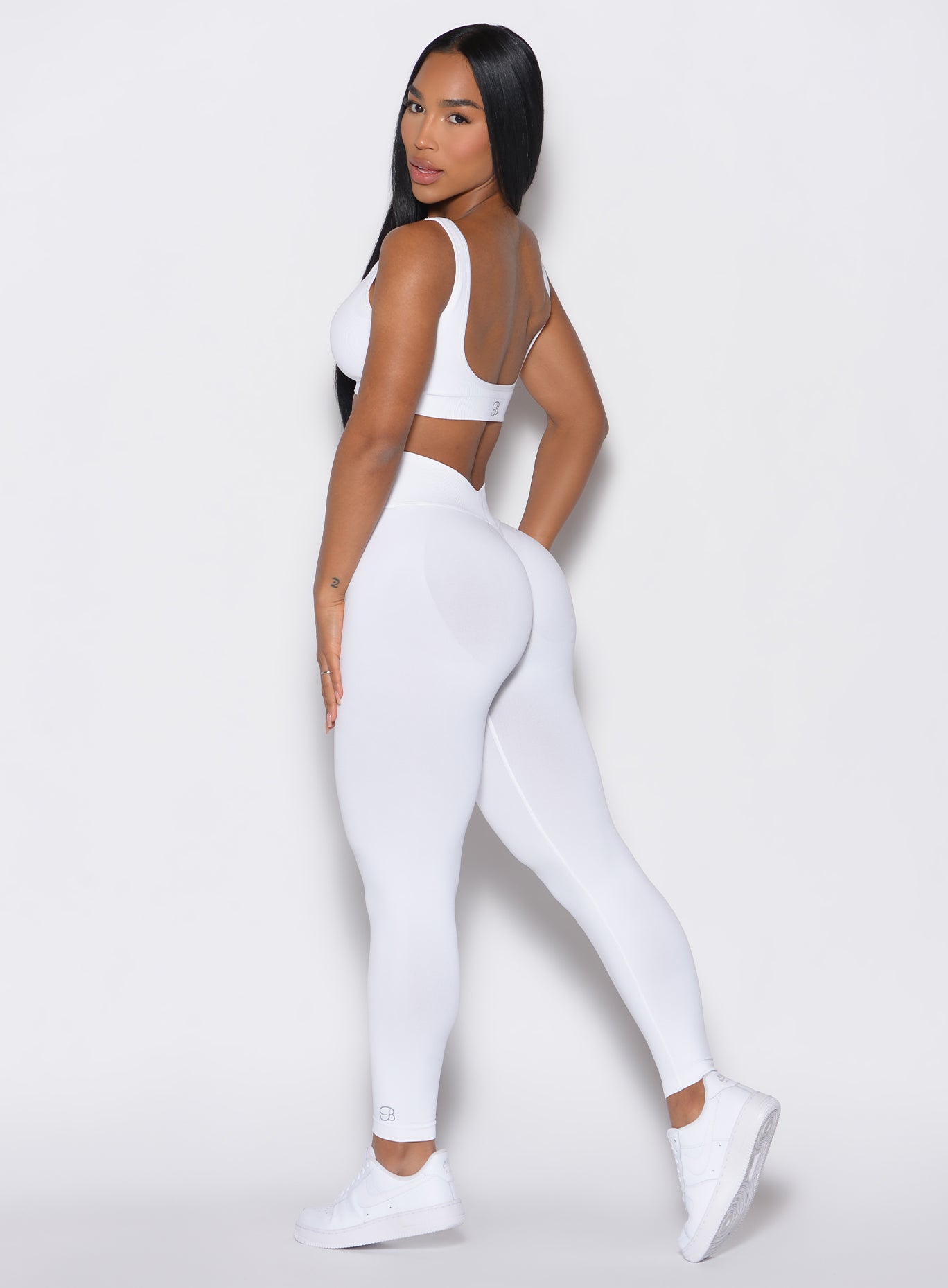left side profile view of a model facing to her left wearing our white V Seamless Leggings along with a matching sports bra