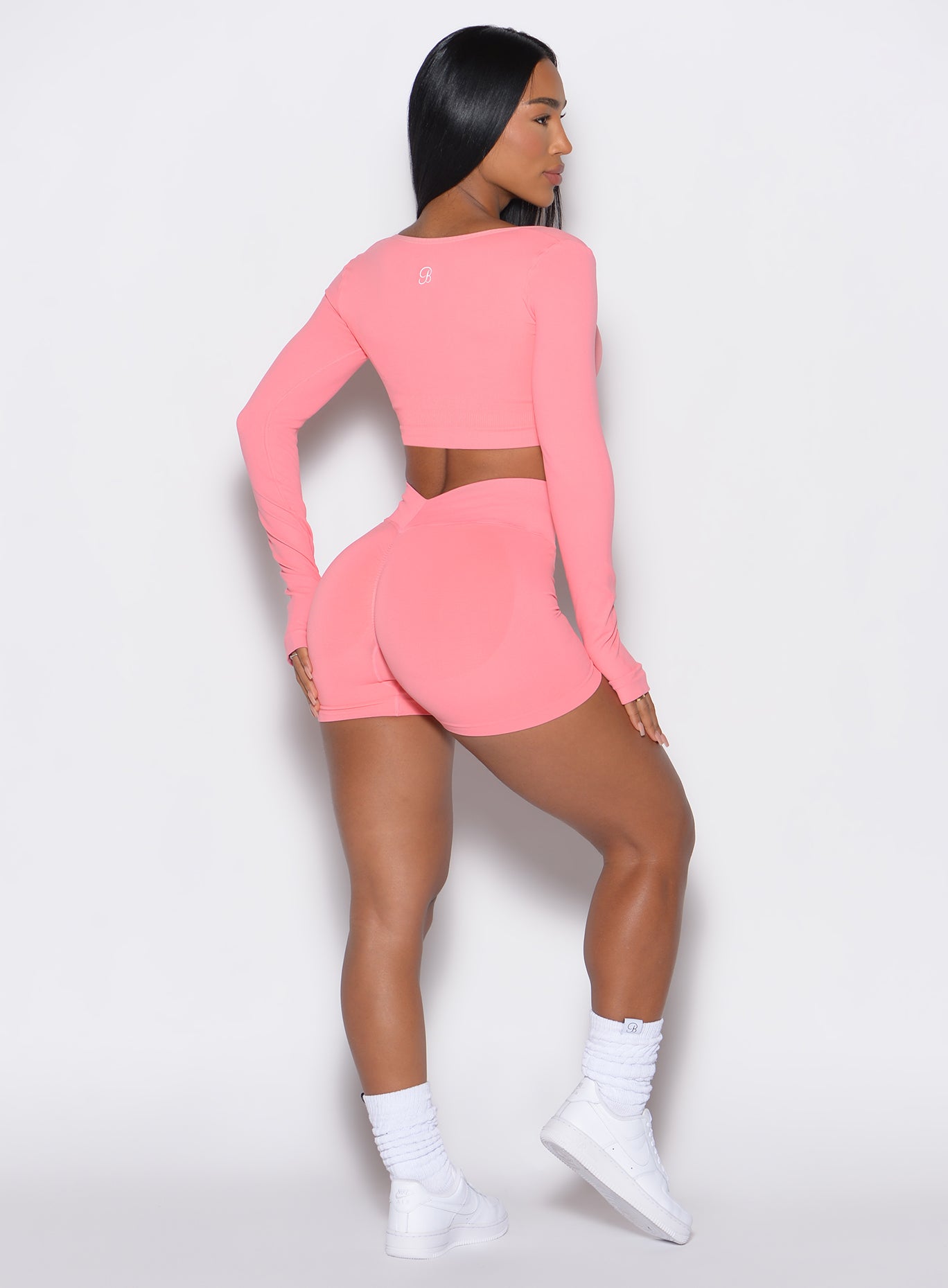 back profile view of a model wearing our v seamless shorts in flamingo color along with the matching pullover 